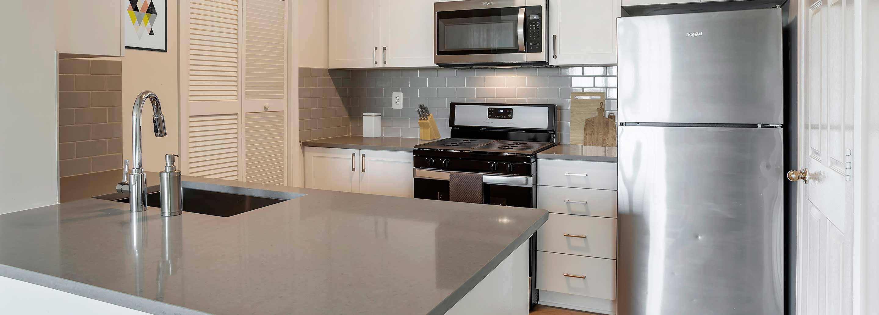 Finish Package II kitchen with white cabinetry, grey quartz countertops, stainless steel appliances and tile backsplash