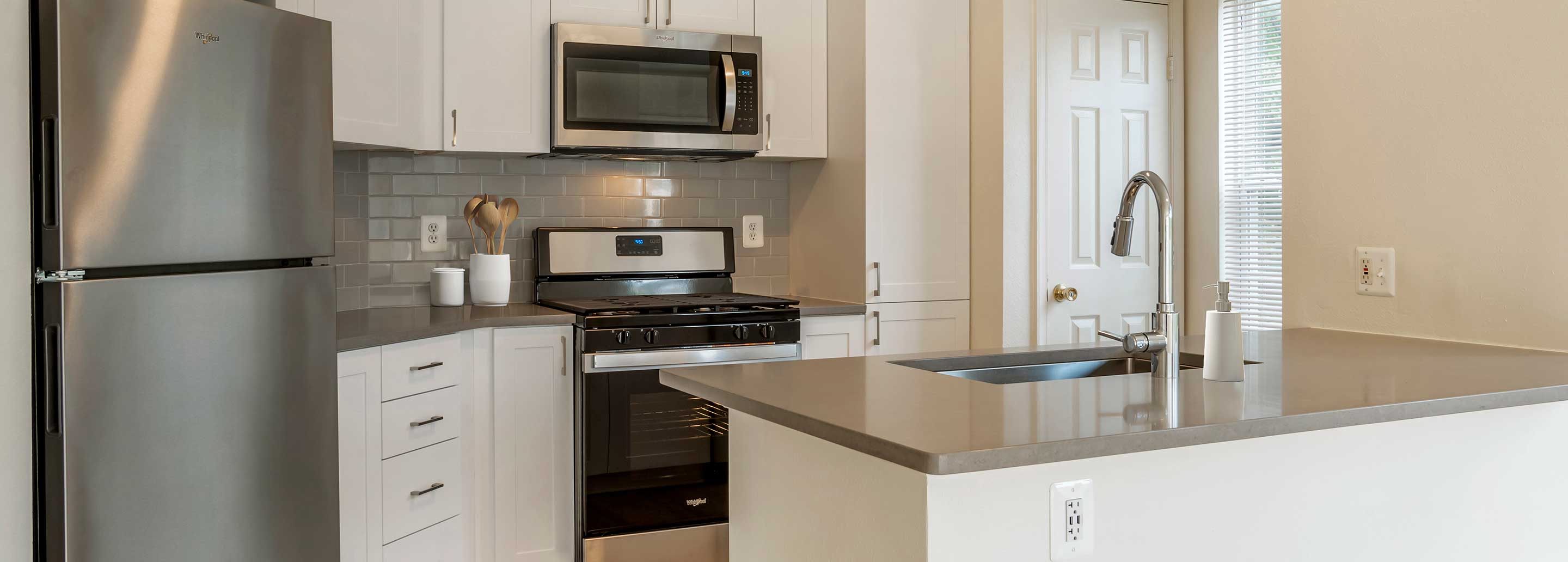 Newly renovated Finish Package V kitchens with white cabinetry, grey quartz countertops, stainless appliances, grey tile backsplash, and hard surface flooring