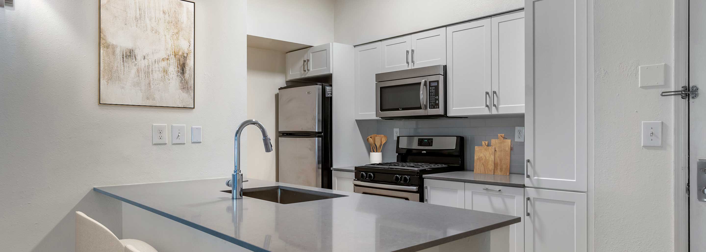 Renovated Package III kitchen with grey quartz countertops, white cabinetry, stainless steel appliances, tile backsplash, and hard surface plank flooring